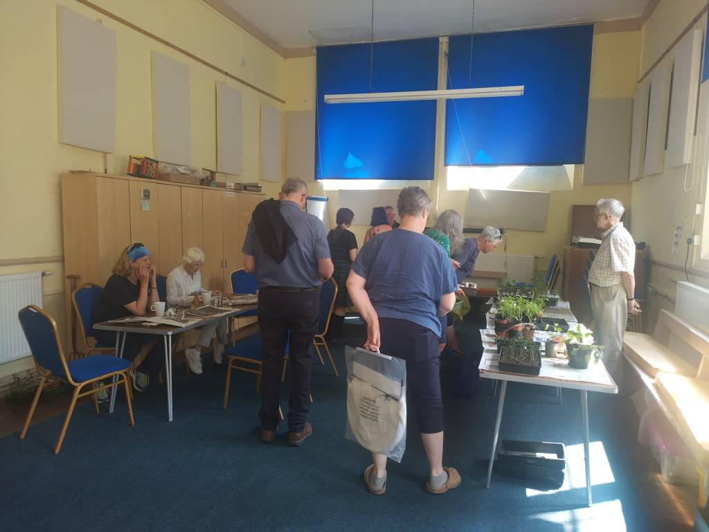 Image of people in a hall looking at a plant stall, making newspaper pots and talking to a volunteer about composting.